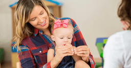 Infant teacher holding a baby and teaching her how to sign "more" using sign language