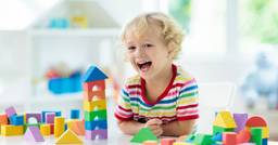 Toddler smiling at the camera and feeling proud after building a tower with foam blocks