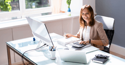 An early childhood director sitting at their desk, behind a computer, with a calculator as they track parent's payments and invoices. 