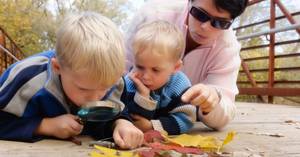 Two toddlers engaging in structured science experienced guided by a teacher involving outdoor observations.