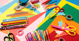 Assortment of colourful art materials, including pink and yellow scissors, crayons, tape, and colourful paper