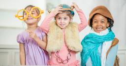 Three girls in preschool smiling at the camera as they play dress up. 